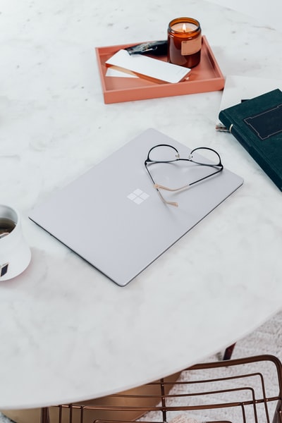 银色微软Surface笔记本电脑3白金，旁边是白色桌子上的黑框眼镜